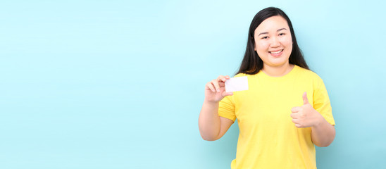 asian woman holding credit card happy with big smile doing ok sign, thumb up with fingers, excellent sign, on a blue background in studio With copy space.