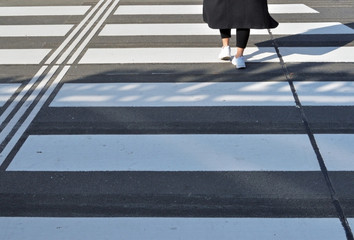 Low section of girl dressed in black and white crossing the street at crosswalk