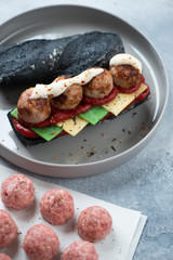 Submarine sandwich with fried meatballs, cheese and black baguette served on a grey plate, vertical...