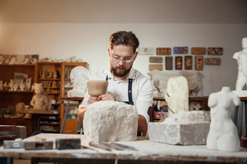 Stone carver works with wooden hammer and chisel at limestone.