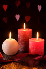Three wax flame candlelight with ribbon in dark romantic light on hearts background, love dating, Valentine's day, selective focus