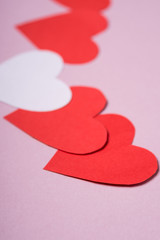 Red and white handmade paper hearts valentines on pink background, angle view, selective focus