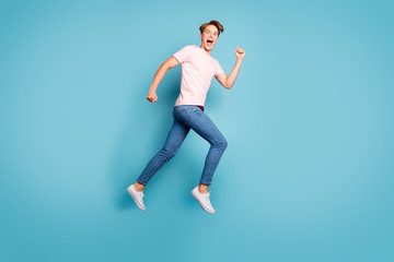 Fototapeta na wymiar Full length profile photo of funny guy jumping high up rushing shopping center low prices addicted shopper wear casual pink t-shirt jeans shoes isolated blue color background