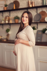Close-up of a young pregnant woman caressing her belly, shot in a white studio. Waiting for the baby, before delivery
