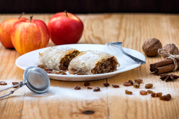 Apple roll pie - Apple Strudel. Pie with apples, cinnamon, walnuts and raisins, sprinkled with powdered sugar in a plate on a wooden table 