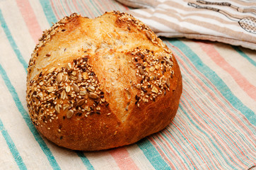 Freshly baked whole grain loaf of bread sprinkled with seeds of flax, sesame, sunflower seeds on linen towel. Home baking. Healthy eating concept. Closeup