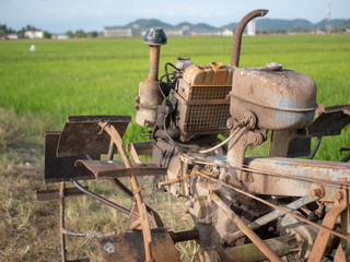 Old and rusty two wheeled tractor or power tiller with paddy field in the background