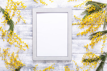 Easter decor with mimosa flowers and frame on wooden table. Mockup with a gray frame. Top view....