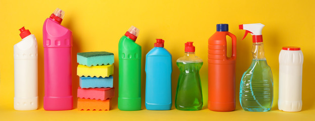 Bottles with detergent and sponges on yellow background, space for text