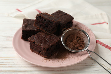 Plate with chocolate cake slices and strainer on wood background with towel, close up