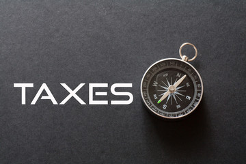 Taxes word written on black background with compass