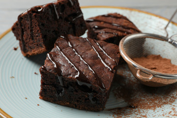 Plate with chocolate cake slices and strainer with powder on wooden background, close up