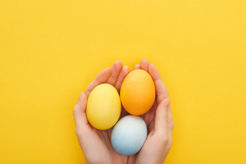 Cropped view of woman holding multicolored painted Easter eggs on yellow background