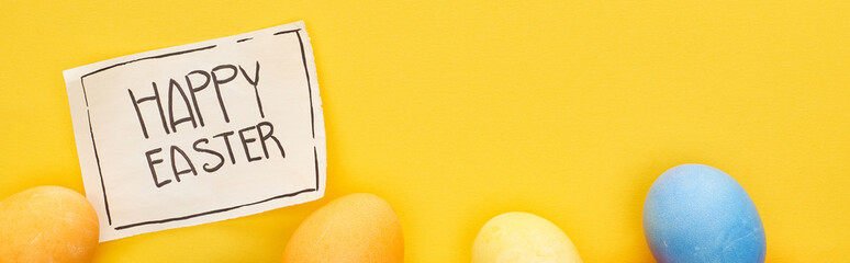 top view of painted eggs and greeting card with happy Easter lettering on yellow colorful background, panoramic shot