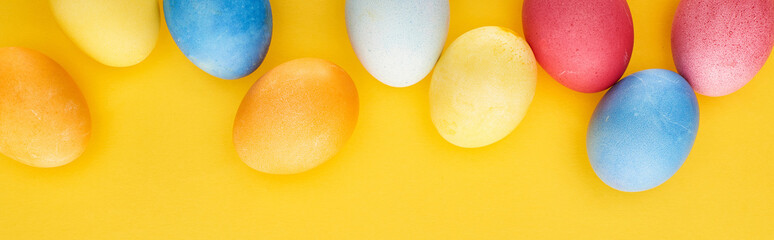 top view of multicolored painted Easter eggs on yellow background, panoramic shot