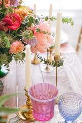 Served table for a wedding dinner in boho chic style. Decor from fresh flowers of peonies, roses, orchids and Leucospermum conocarpodendron. Crockery plates, glasses and candles. Wooden table.