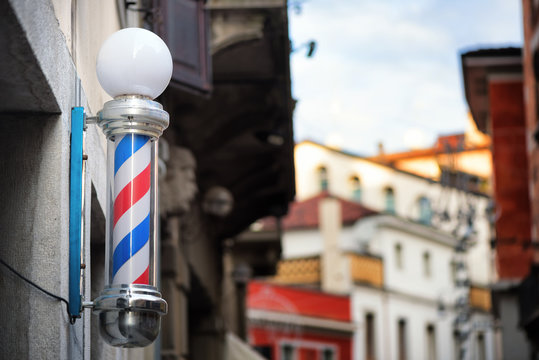 Barber shop pole with defocused Italian architecture in background. Udine city, Friuli Venezia Giulia region, Italy.