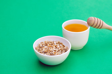 A plate of granola with honey and a spoon on a green background.