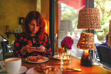 A young girl is sitting in a cafe with a phone.
