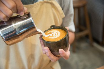 Barista pouring milk in to coffee cup making beautiful latte art.Coffee latte art in coffee shop