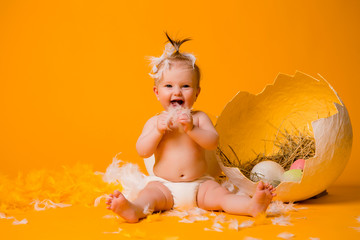 baby girl in a chicken costume with feathers and Easter eggs on a yellow background, space for text. the concept of Easter