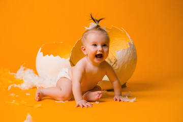 baby girl in a chicken costume with feathers and Easter eggs on a yellow background, space for...