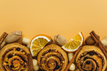 Cinnamon rolls, raisins and nuts. Pecans, peanuts and lemon slices on orange background with copy...