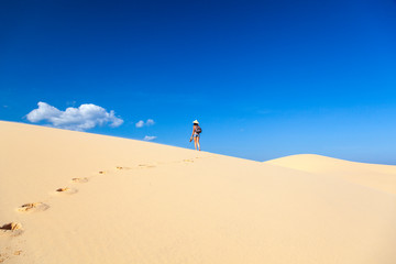 Fototapeta na wymiar beautiful girl in the desert goes on a hill barefoot on the sand with a hat and shoes in her hands