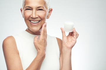 Gorgeous smiling Caucasian senior woman trying out new anti age cream and looking at camera. Beauty...