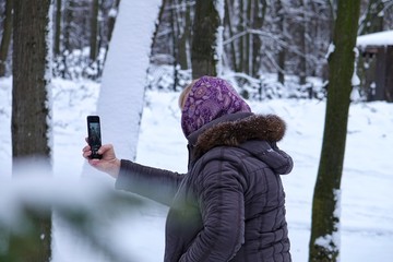 Fototapeta na wymiar Woman takes pictures on the phone in a snowy park
