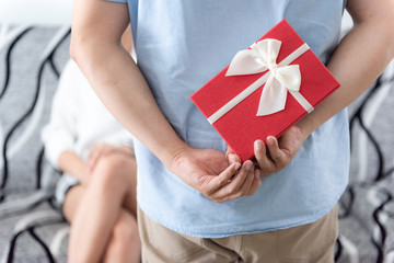 Surprise couple. A young man a good mood holds a gift box hidden behind.  