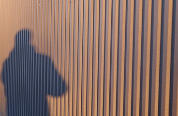 Man's shadow on a corrugated fence, background