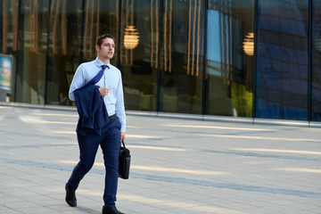 Tired young businessman with case going after work in hot wheather