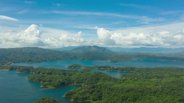 Clouds over a blue lake among green hills and mountains covered with rainforest.Time lapse.