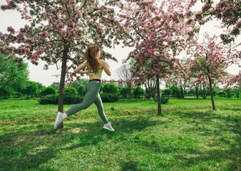 Obraz na płótnie Canvas 1 white woman with long hair in sports leggings and a top, sneakers, a girl running through a spring blooming Apple orchard