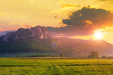rock formation on the field at sunset. beautiful rural landscape in mountains. wonderful scenery in spring. clouds on the blue sky in evening light. forest on the hills