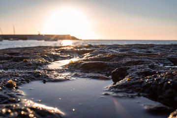 atardecer en un puerto con rocas y reflejos en primer plano