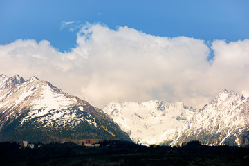 high tatras mountain ridge in springtime. snow capped rocky peaks in dramatic dappled sunlight beneath a clouds on a blue sky. place where earth meets sky concept