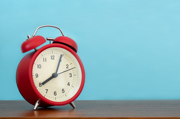 Red alarm clock on wooden table and light blue color background 