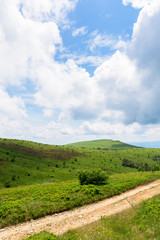 mountain dirt road scenery. path through the grassy meadows on rolling hills. ridge in the distance. green carpathian landscape. cloudy summer weather. dramatic sky