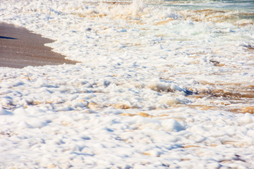 sea waves splash foam on the sunny beach.  mess of salt water and sand in evening light. dynamic nature texture