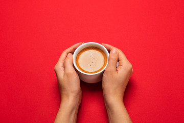 Female hand holding a white cup with black coffee on a red background.