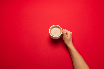 Female hand holding a white cup with black coffee on a red background.