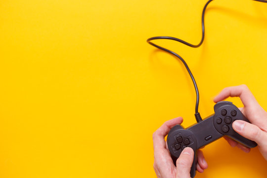 Man holding wired gamepad or video game controller on yellow background. Top view, flat lay