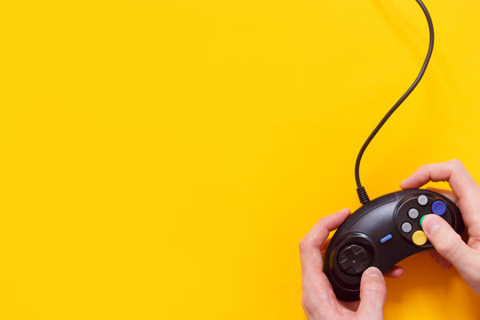 Man holding wired gamepad or video game controller on yellow background. Top view, flat lay