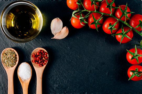 Dark background of colorful food ingredients : fresh cherry tomatoes, garlic, bread, spices tablespoons. healthy mediterranean diet.