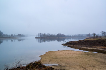 Abandoned place landscape, early morning fog. Calm water, misty lake background.