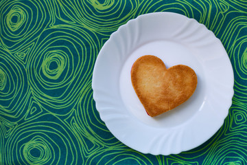 Tasty heart-shaped cookie, for Valentine's Day, prepared on a white plate on an abstract blue background.