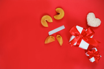 Valentine's day celebration concept. Two gifts in white packaging with a red bow on a scarlet (red) background. Fortune cookies and white heart made of cotton yarn. Greeting card for the holiday.