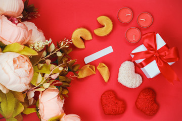 Valentine's day celebration concept. A bouquet of pink ranuluxus, a gift in white packaging with a red bow on a scarlet background. Scented candles and fortune cookies. Three cotton hearts.